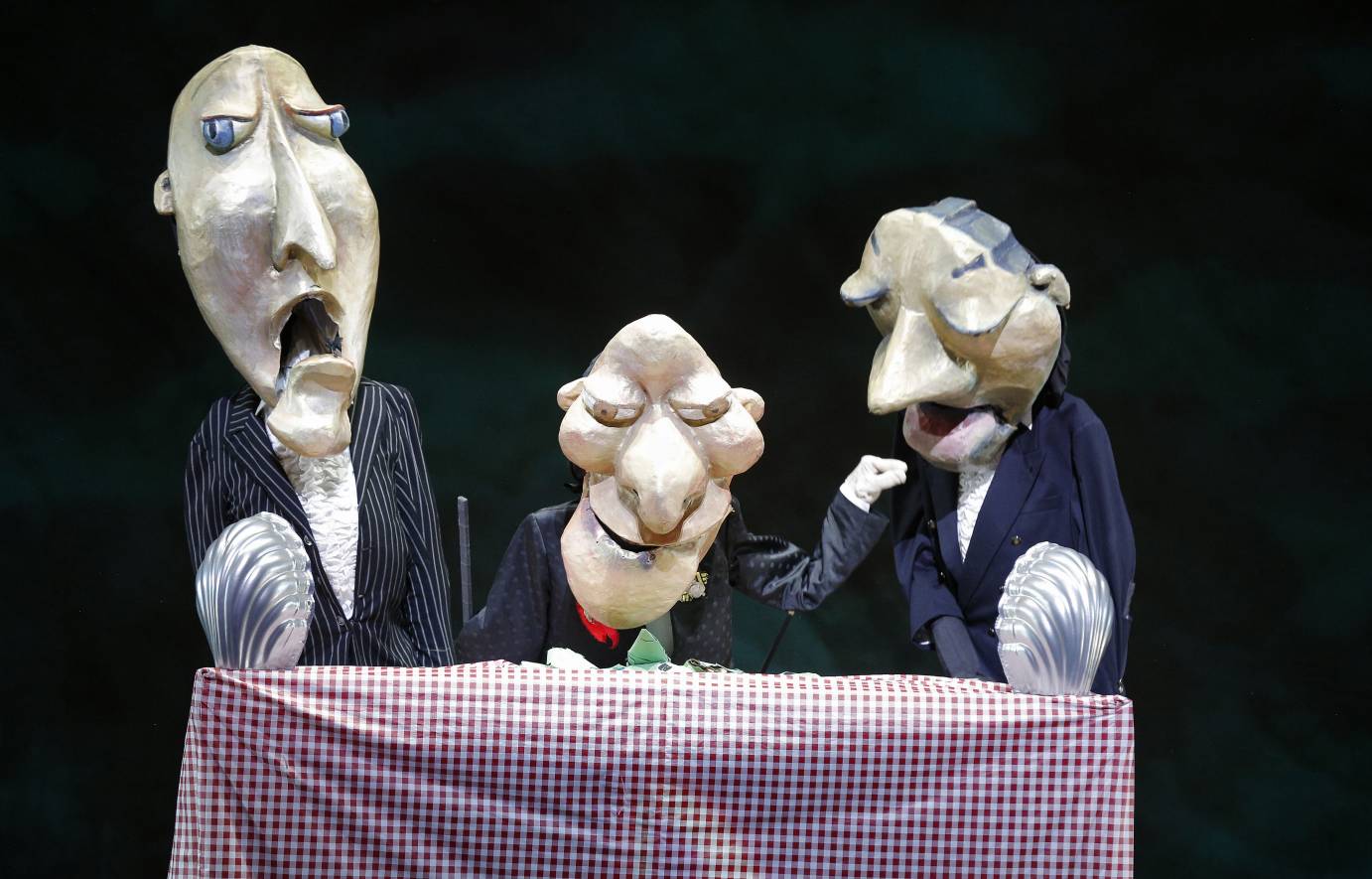 Three big-headed puppets sit at a table