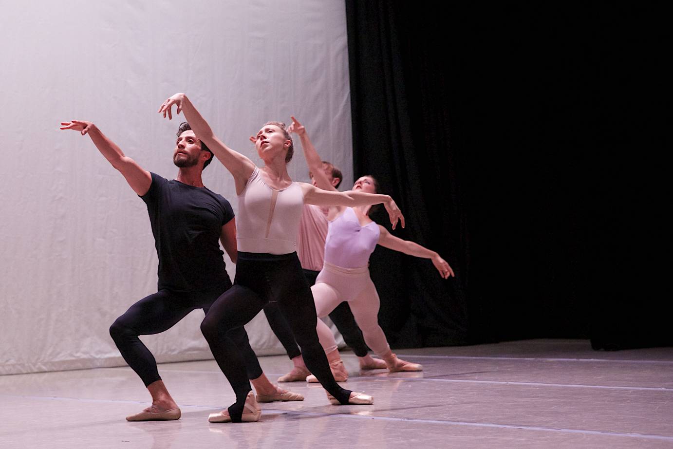 Four people in ballet practice clothes lunge with arabesque arms