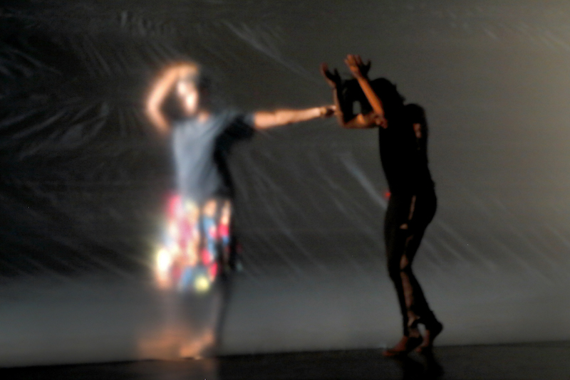 A woman dances behind a plastic sheet and another dances in front of it