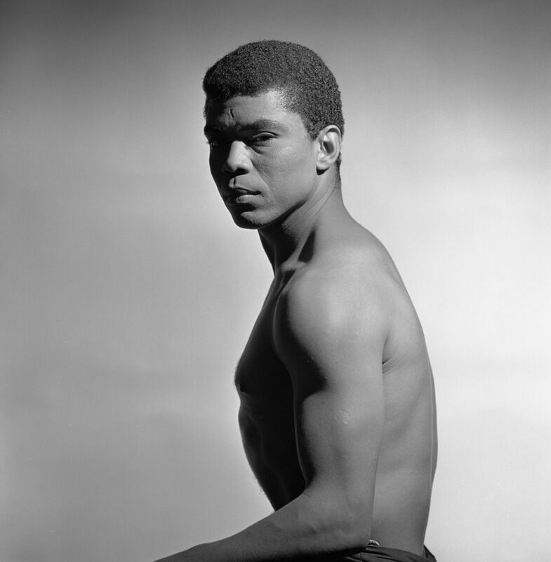 A young Alvin Ailey. His bare-chested body is in profile but his somber face is turned to the camera