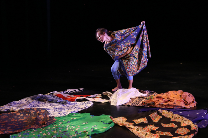 woman surrounded by mu mus of various colors and patterns manipulates one as she dances in it