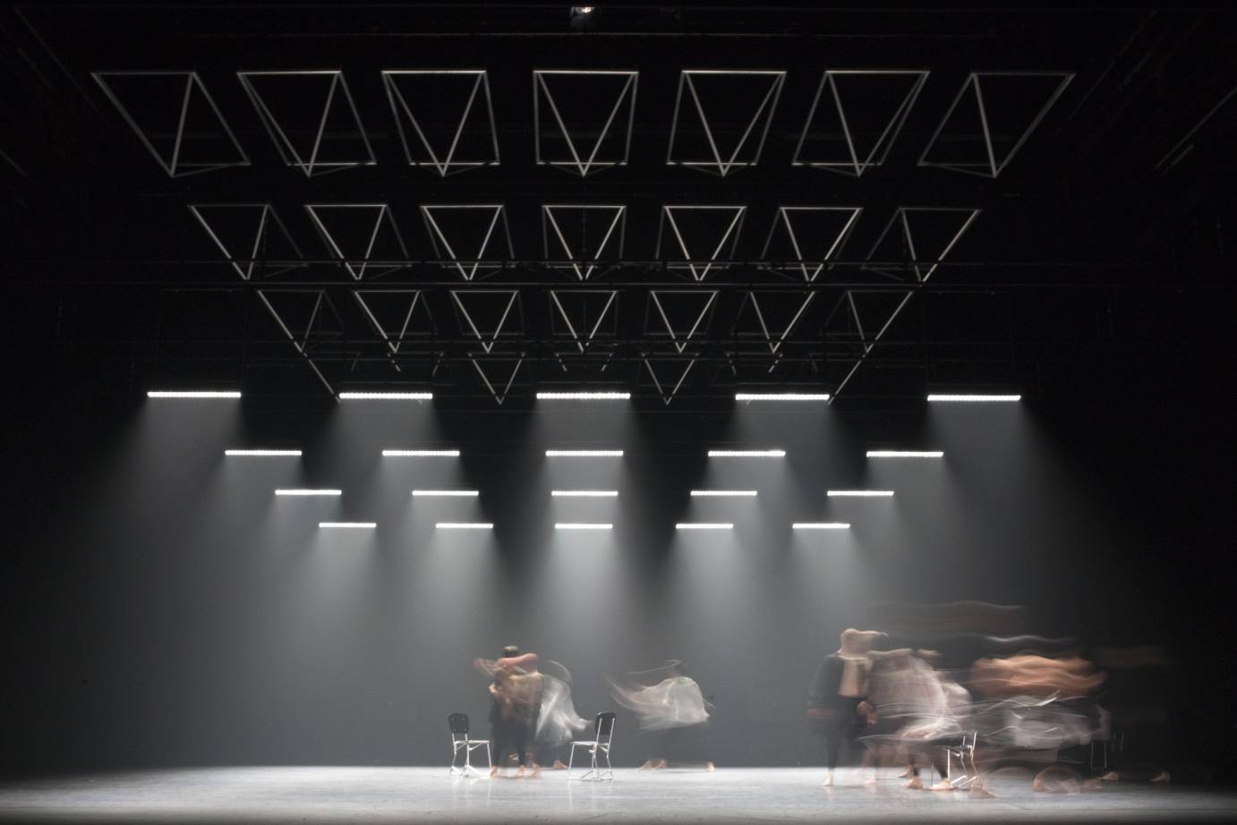 A blurred image of dances and chairs illuminated by strips of lights.