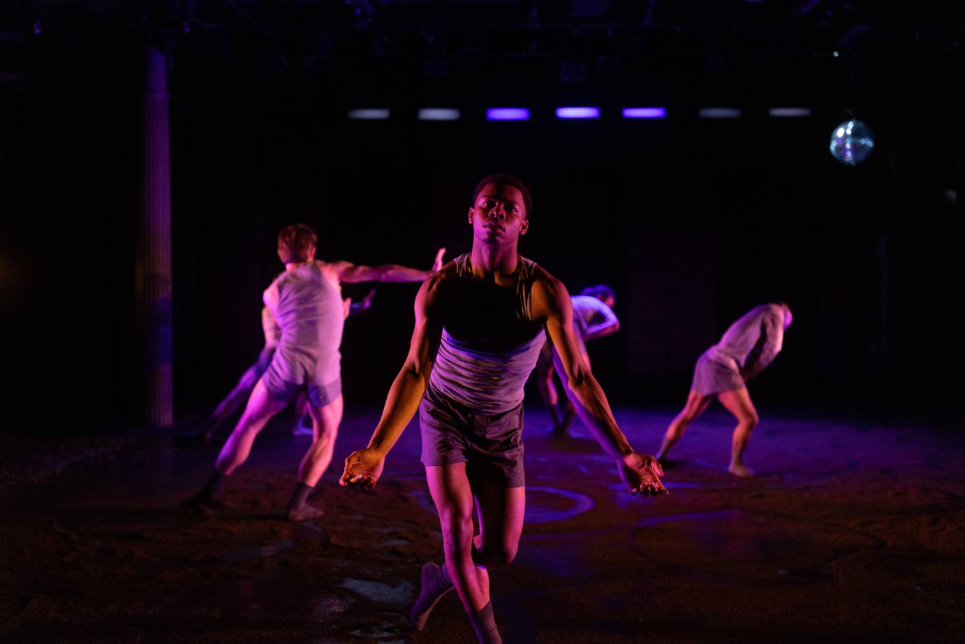 a disco ball hangs to one side, as a dancer in gray shorts and songs look outs to us, as if mid bow, but he is not he seems that he pleading for our sympathy or empathy... 