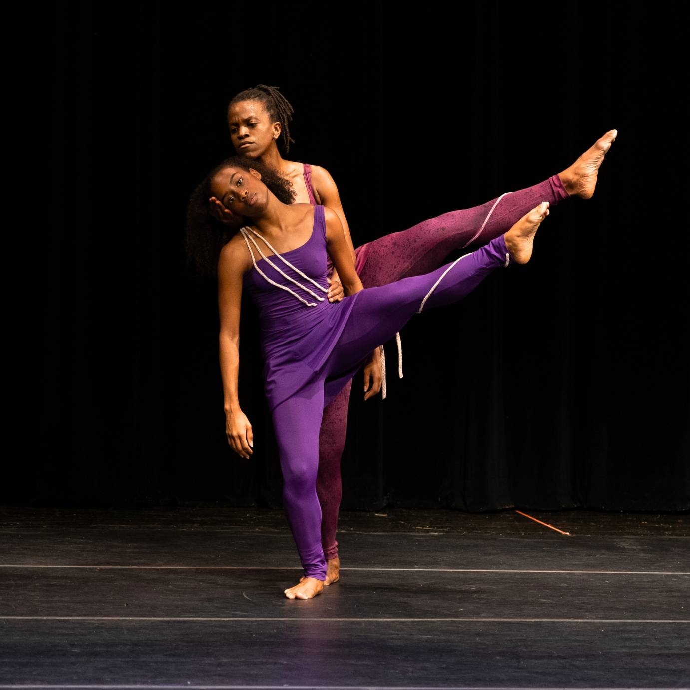 Two women, one taller are in unison standing on their right legs while their left legs stretch long ala seconde.