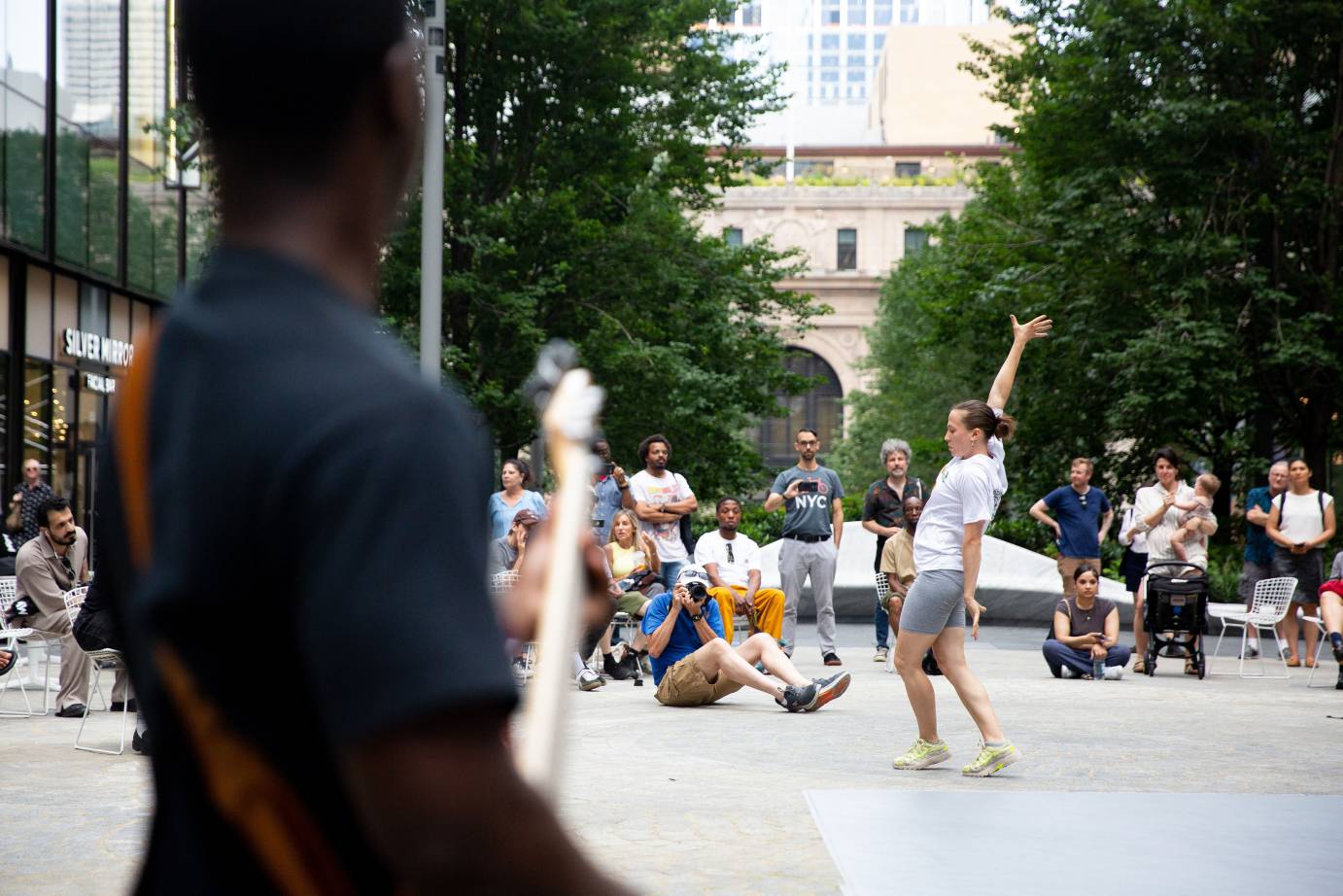 an artist in shorts and heels dances in the plaza as on lookers gather round 