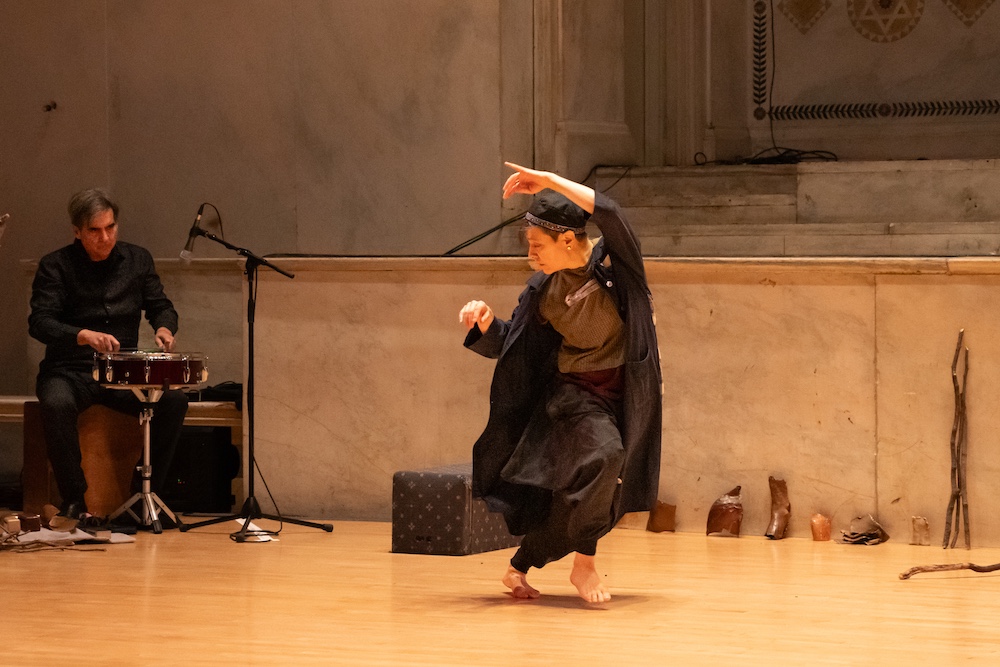 a dancer leaning into a step as a drummer looks on