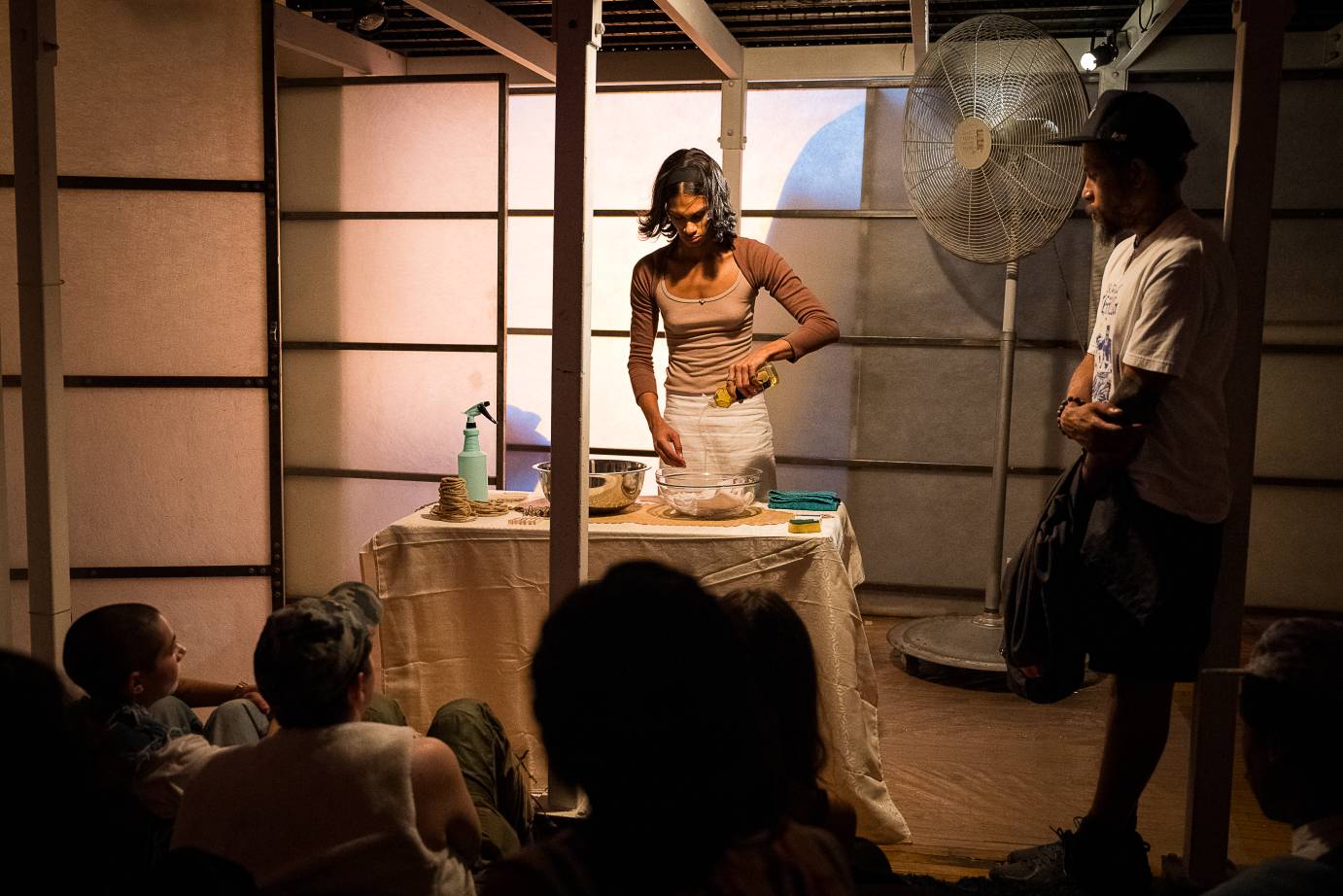 in an installation resembling a home artisy ms z tye stands at a table doing household chores as an audience member looks on