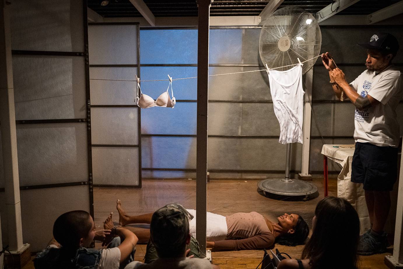 an audience member holds the end of a clothes line from which a bra and a white t-shirt hang, ms z tye lies under the clothes line 