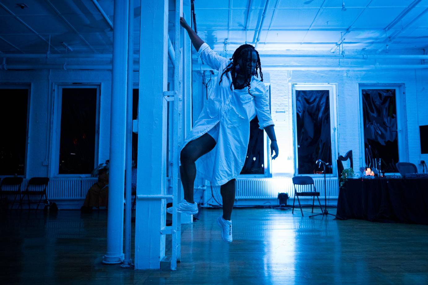 in cool blue light Ogemi Ude  in white sneakers and an oversized white shirt, climbs down from a ladder  installation