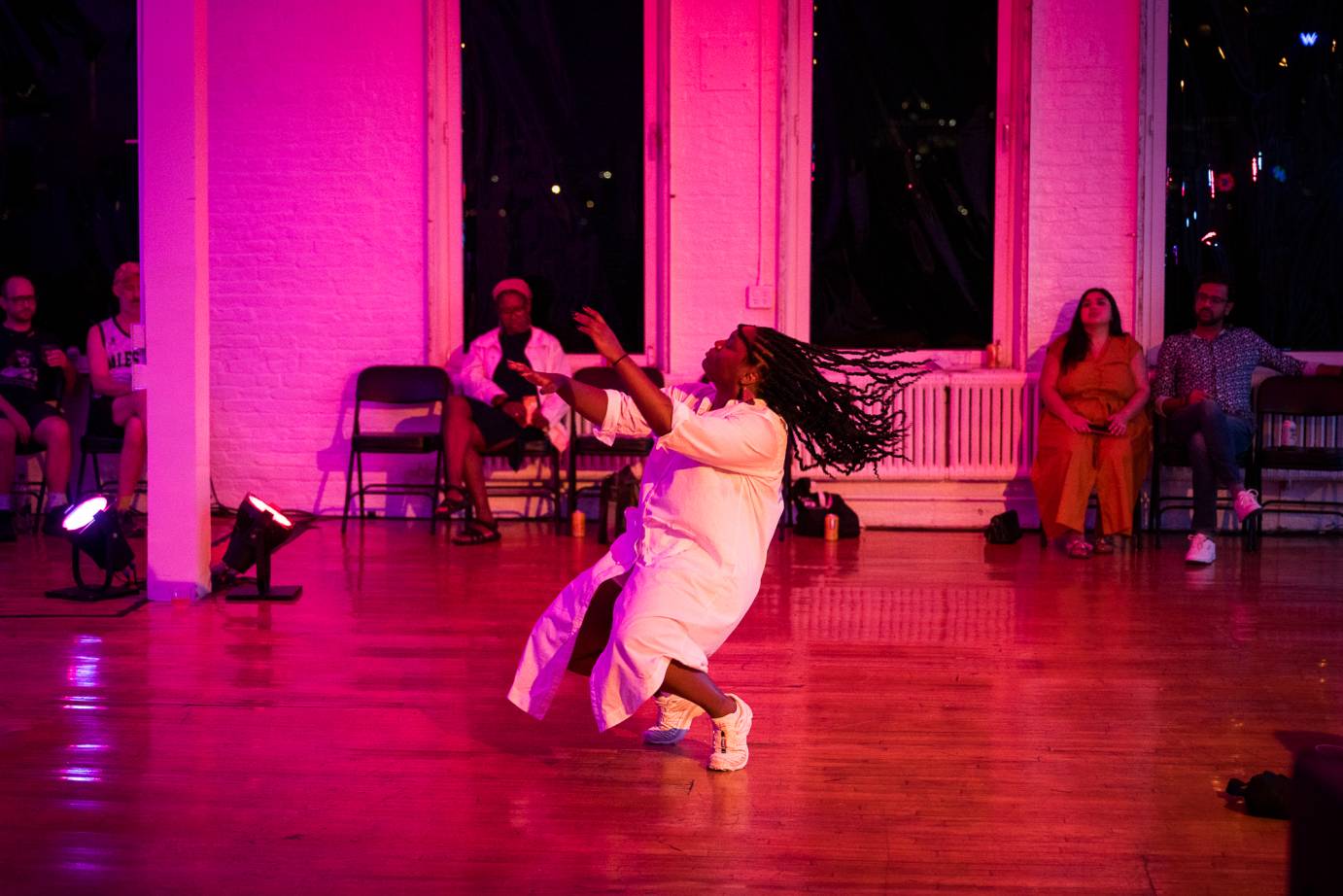 in pink light with audience members around the walls of the loft Ogemi Ude is caught as if moving into  a kneeling lean backwards in the center of the floor