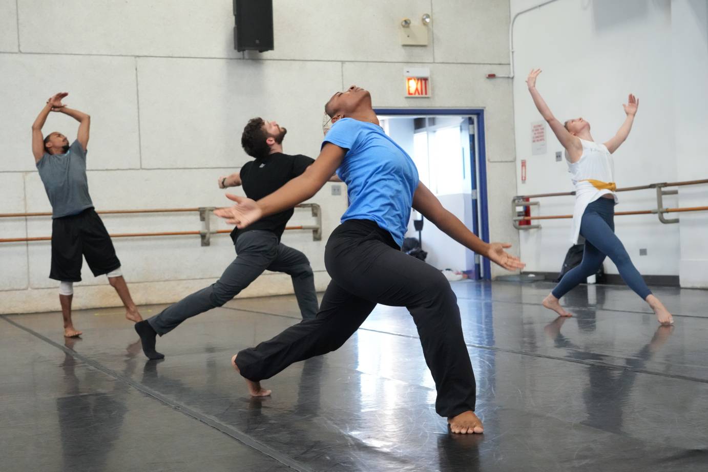 four dancers in rehearsal facing different directions in the room and holding different shapes expressing grief 