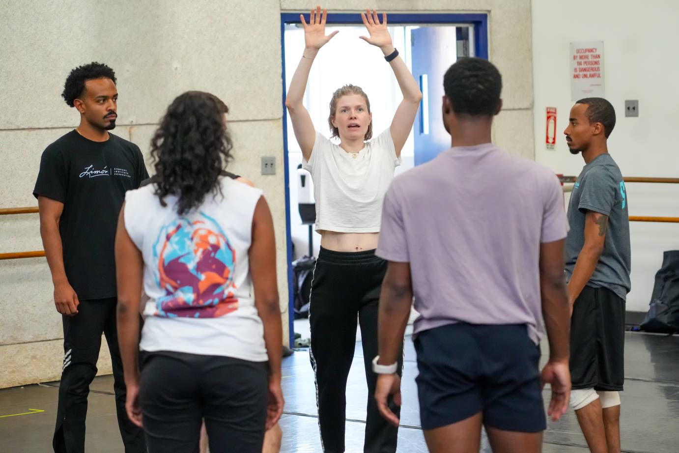 the dancers hover around the rehearsal director whose arms are extended over her head framing it with a diamond shape