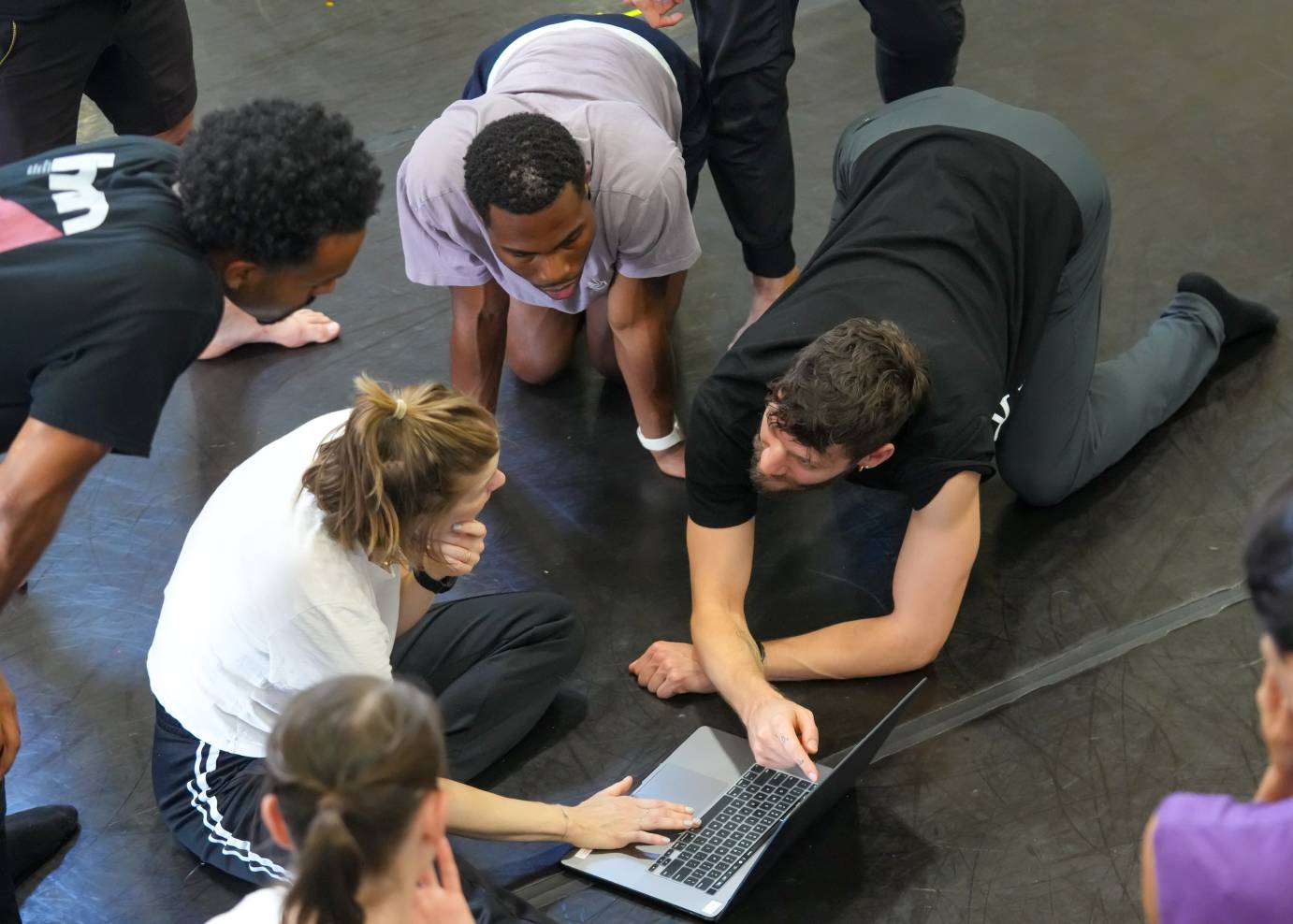 the dancers huddle around the computer to look at the video of the dance for notes 