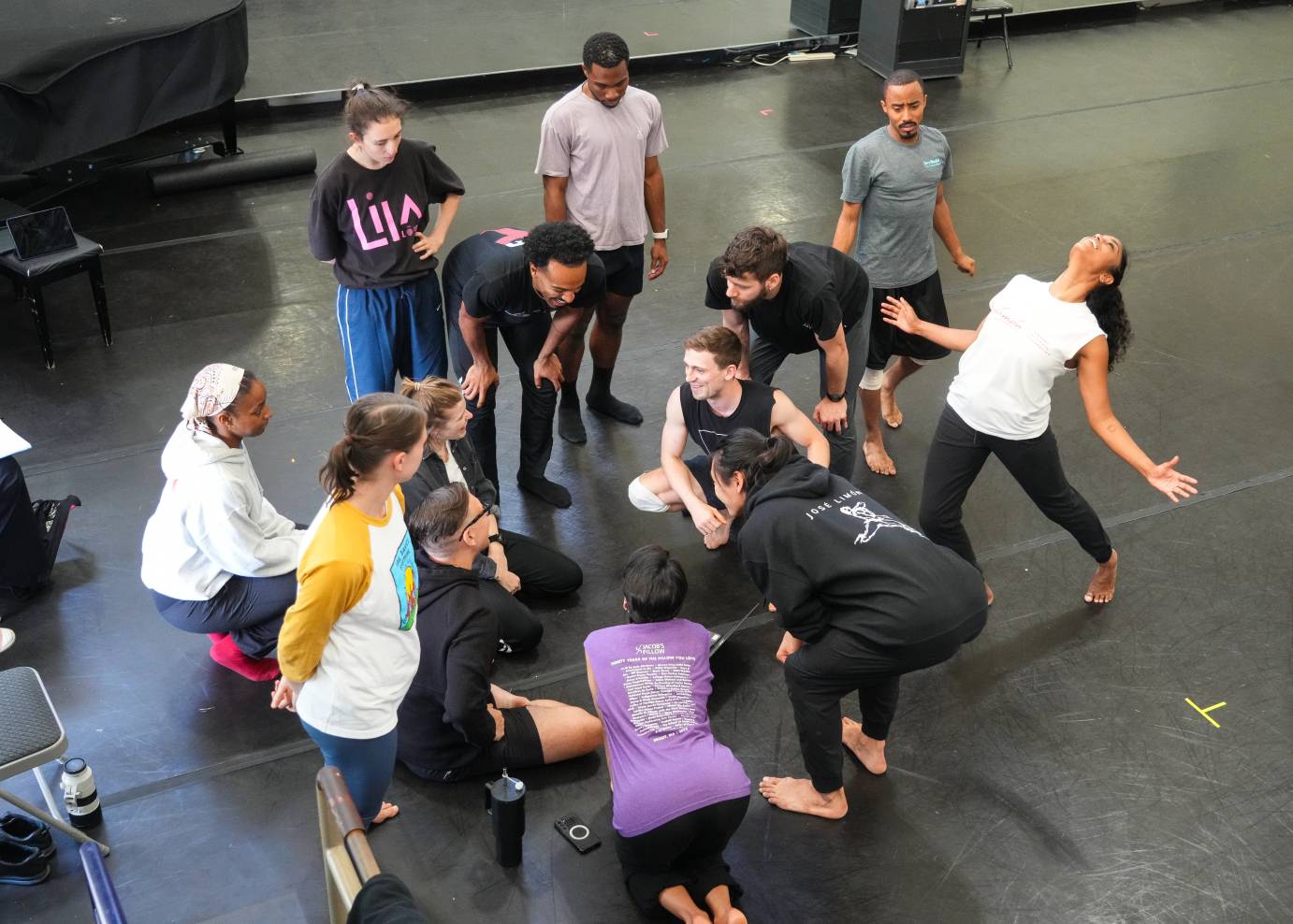 the dancers gather around the artistic directors and seem in good spirits laughing with one another some standing some kneeling on floor some sitting others posing 