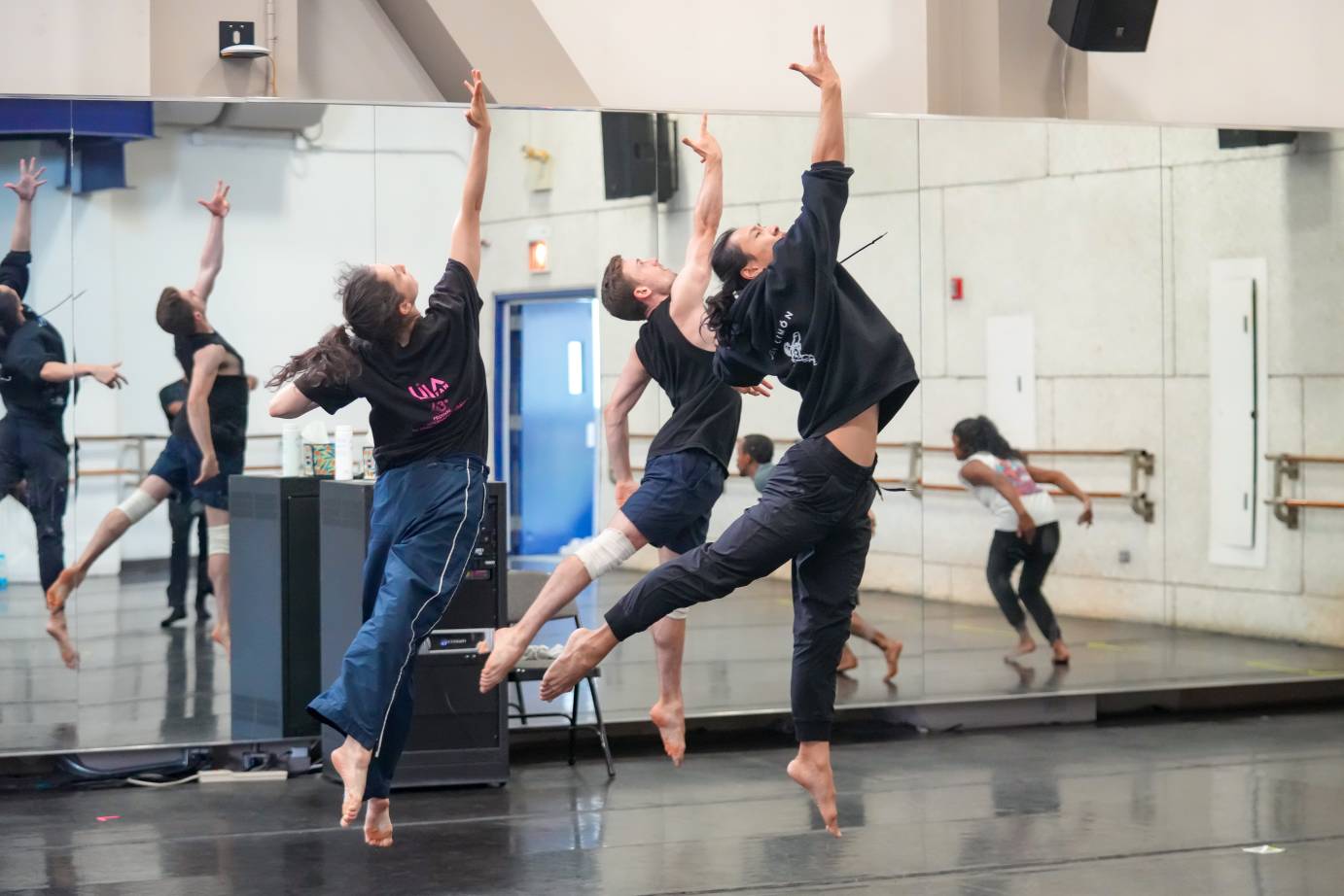 three dancers in sweats and t-shirts leap high into the air hanging there in an arabesque position 