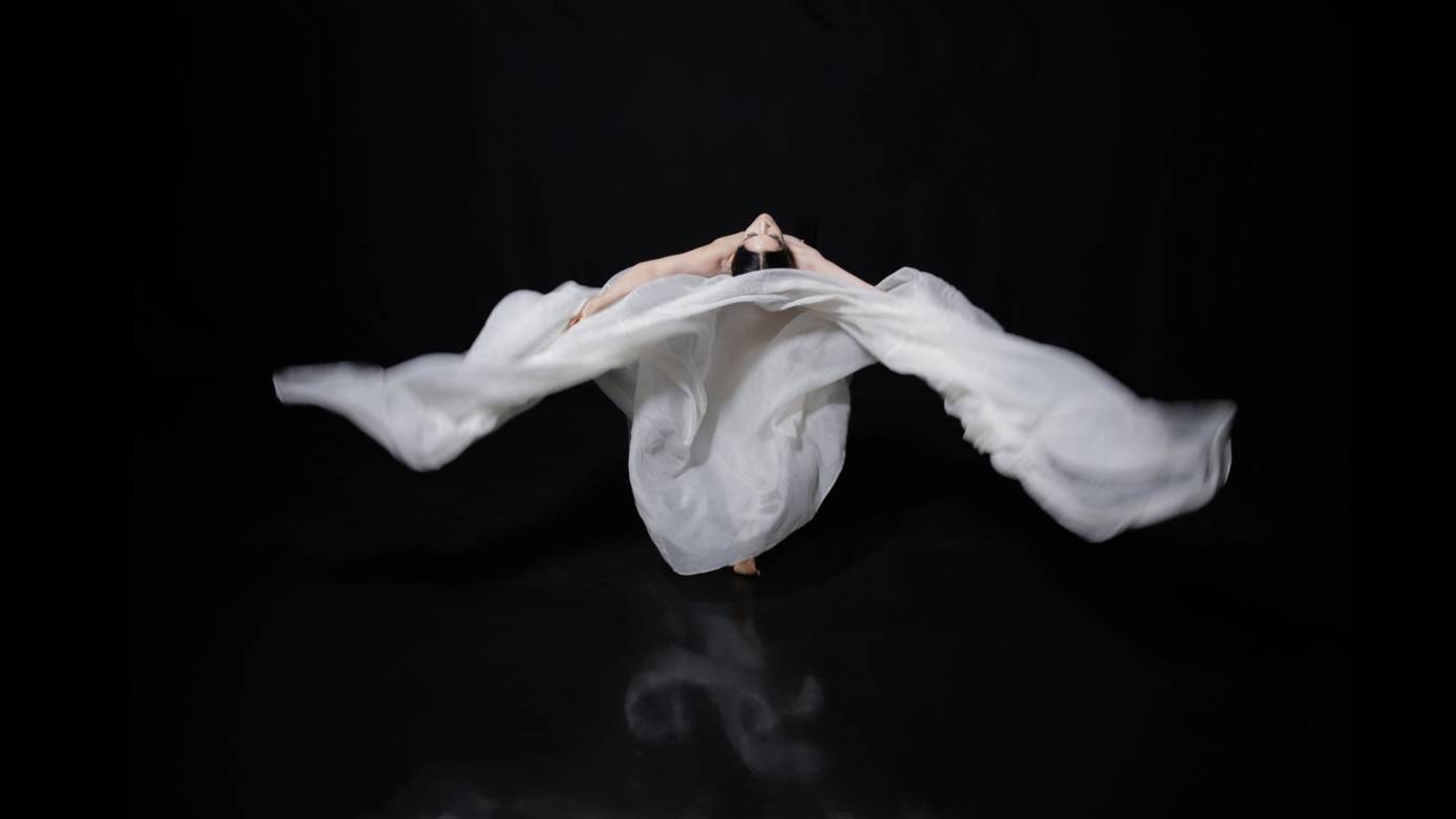 A woman swathed and enveloped in flowing fabric bends backward toward the viewer.