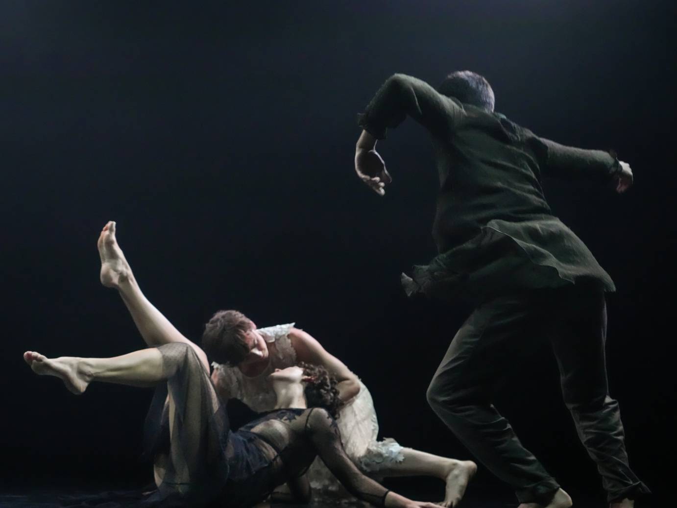 Two dancers tumble toward the floor while a third dressed all in black looms nearby