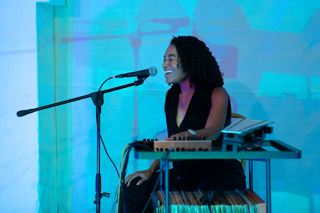 Eyes closed, a sitting woman sings into a microphone.