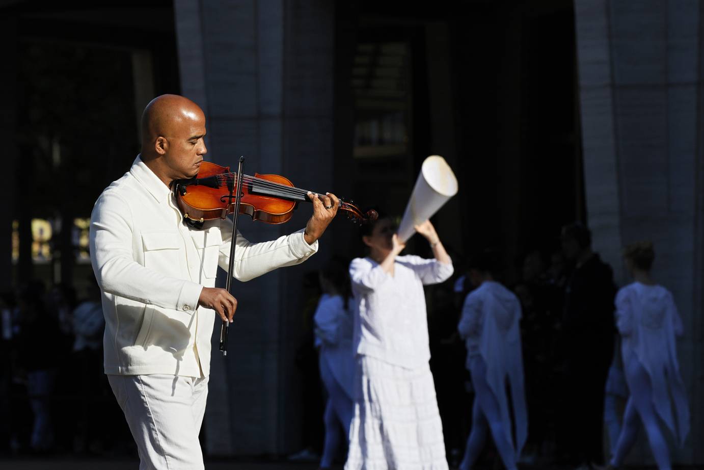 Violinist Daniel Bernard Roumain walks around the fountain playing his violin