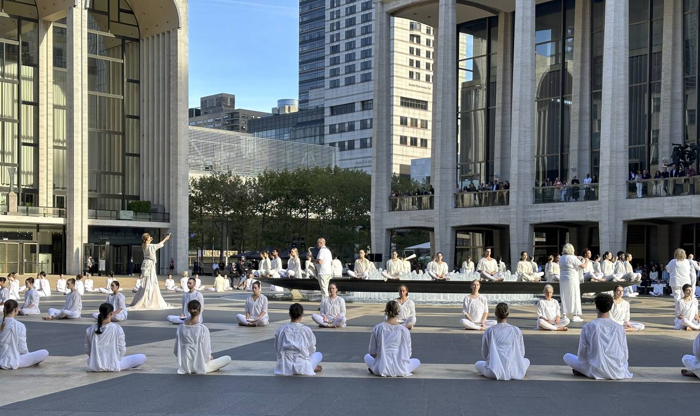 a mass of dancers in white, seated in circles around Revson Fountain at Lincoln Center