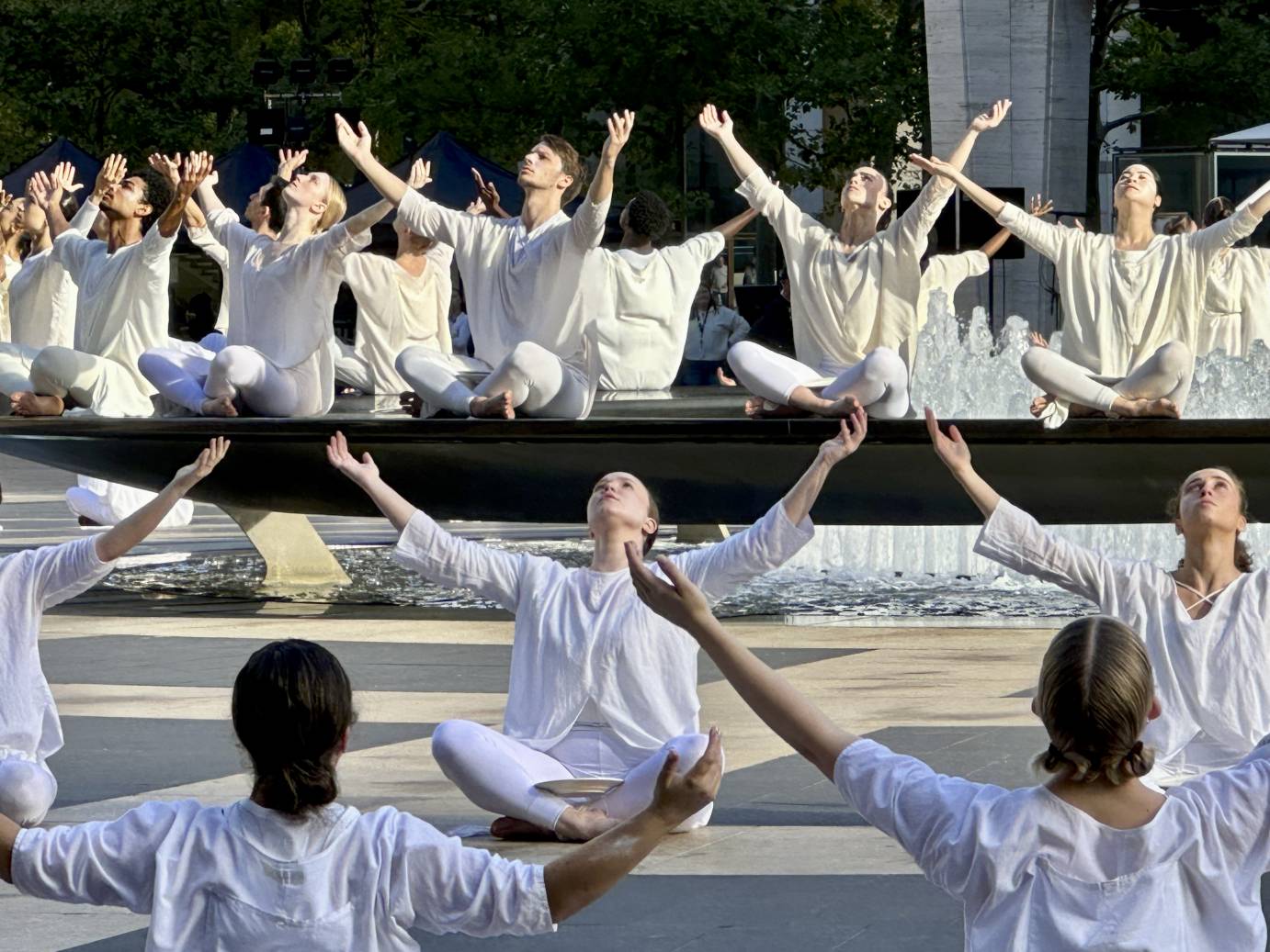 the cast of Table of Silence seated around Revson Fountain lifting their arms, towards the sky