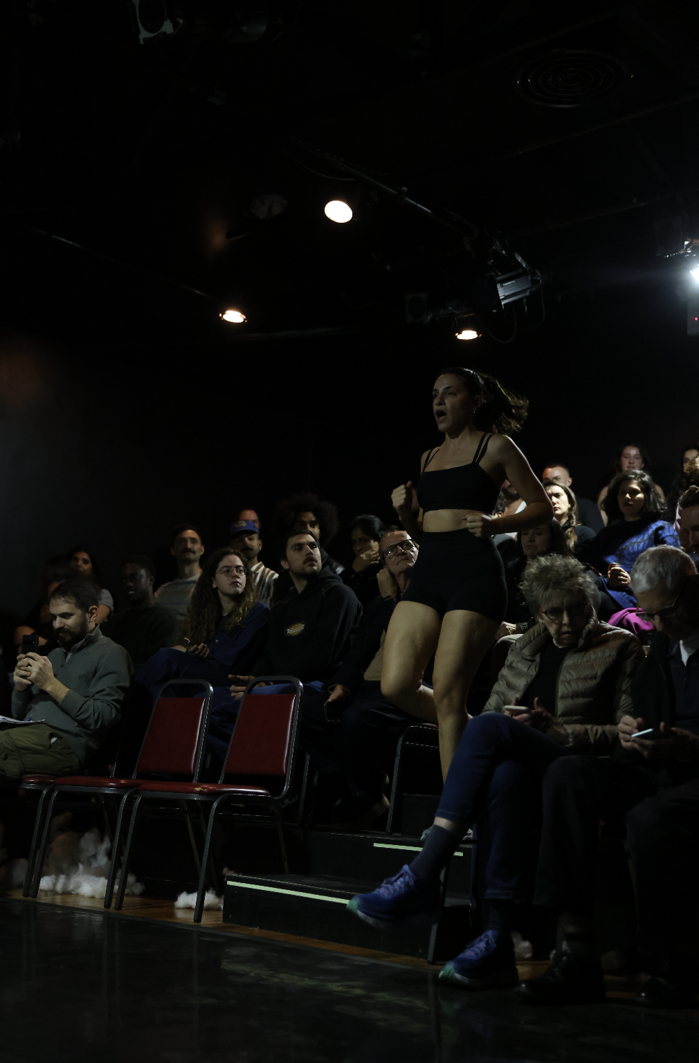 a woman in jogging shorts and a sports bra runs through the audience her ponytail bouncing behind her