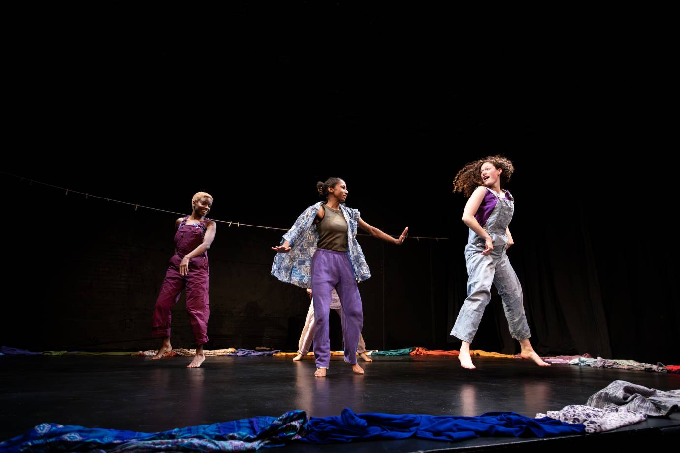 clothes on the floor in a semi circle are being danced around by three jubilant  gals in casual clothes 